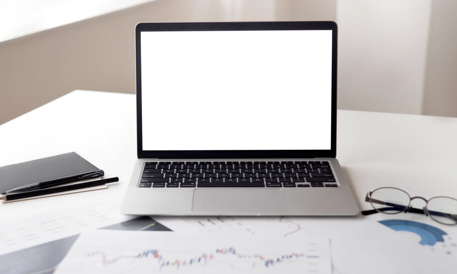 A laptop beside financial papers and reading glasses on a desk.